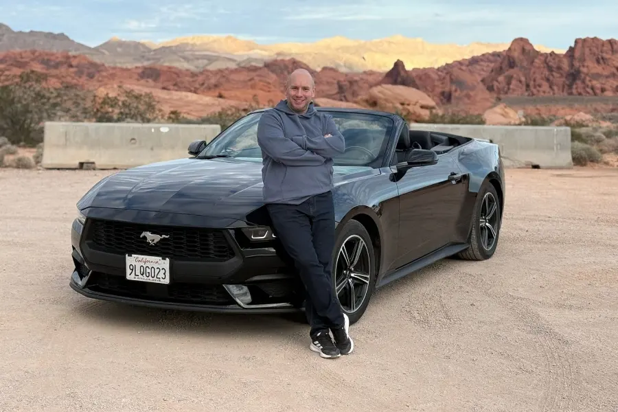 Lee Brooker leaning against a black Ford Mustang convertible in the Nevada desert.