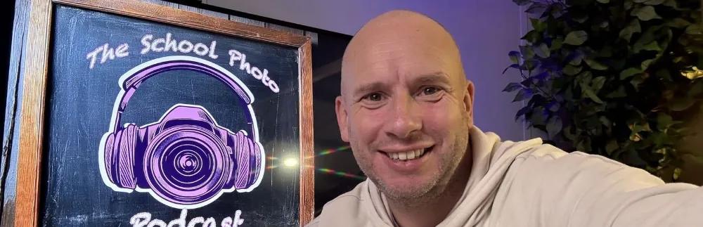 Lee Brooker beside a chalkboard drawing of The School Photo Podcast logo.