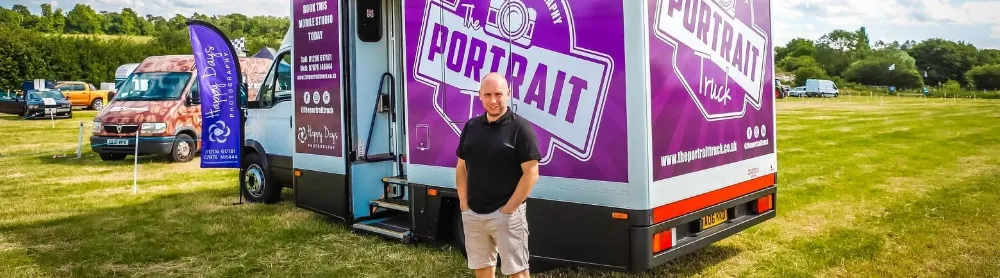 The Portrait Truck, the Happy Days Creative mobile studio, parked on grass with Lee Brooker standing beside it.